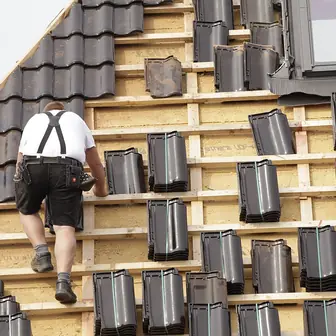 A roofer laying tiles on a pitched roof