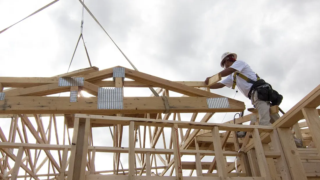 Construction workers framing a house in fall-protection harnesses